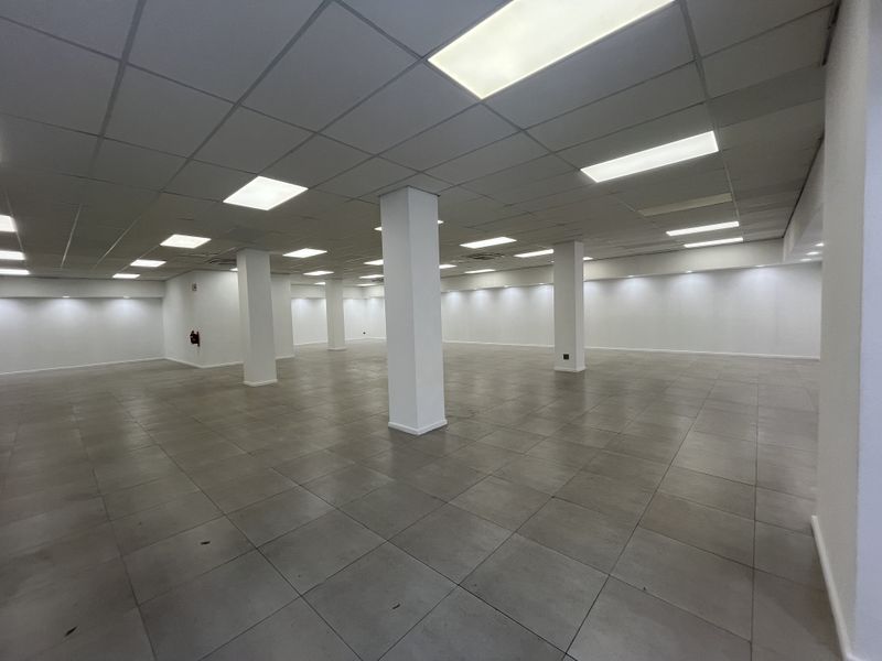 A spacious, open-plan retail area featuring neutral tiled flooring, structural support columns, and a suspended ceiling with integrated recessed lighting.
