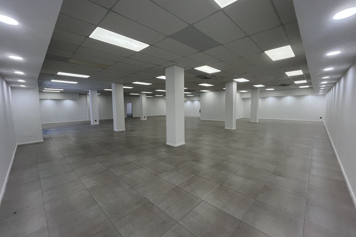 Spacious open-plan retail area featuring neutral tiled flooring, structural support columns, and a modern suspended ceiling with integrated recessed lighting.