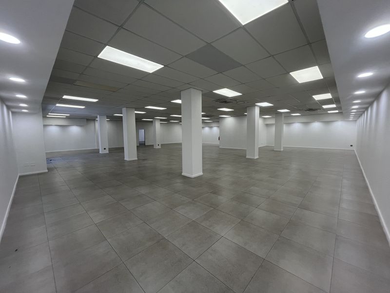Spacious open-plan retail area featuring neutral tiled flooring, structural support columns, and a modern suspended ceiling with integrated recessed lighting.