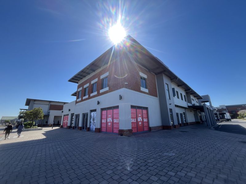 A modern multi-story retail building featuring a brick and plaster facade with large display windows, situated on a paved commercial lot.