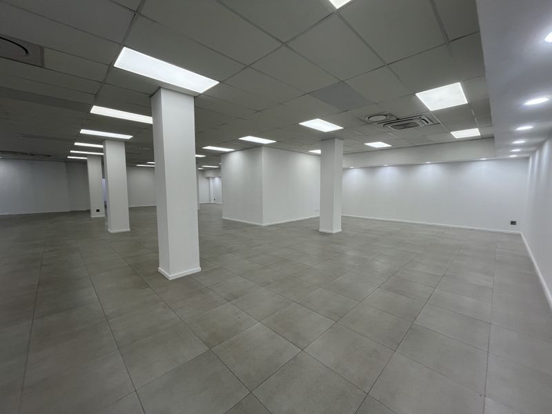 A spacious, open-plan retail area featuring neutral ceramic floor tiles, a modern suspended ceiling with recessed lighting, and structural support columns.