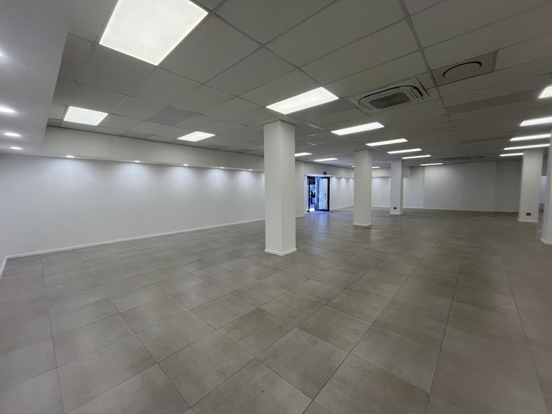 A spacious, open-plan retail area featuring neutral tiled flooring, structural columns, and a modern suspended ceiling with integrated lighting and air conditioning.