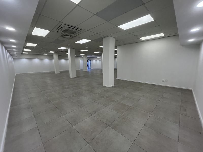A spacious, open-plan retail area featuring neutral ceramic floor tiles, a modern suspended ceiling with recessed lighting, and integrated cassette air conditioning.
