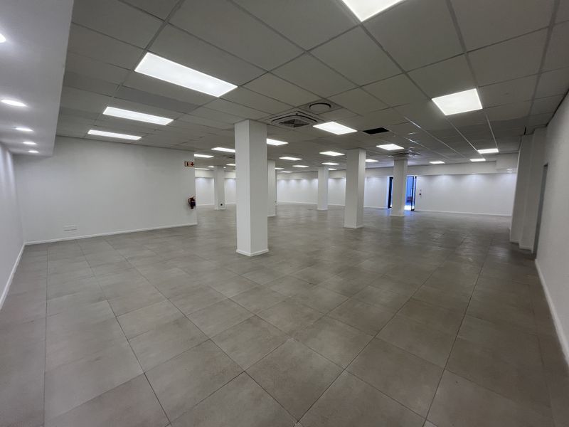 Spacious open-plan retail area featuring neutral ceramic floor tiles, suspended ceiling with recessed lighting, and structural support columns.