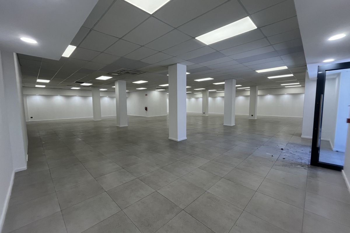 Spacious open-plan retail area featuring neutral tiled flooring, structural columns, and a modern suspended ceiling with recessed lighting.