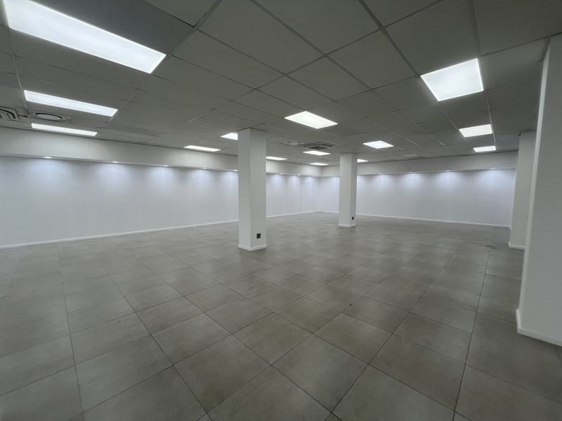 A spacious, open-plan retail area featuring modern ceramic floor tiles, a suspended ceiling with recessed LED lighting, and clean, white-painted walls.