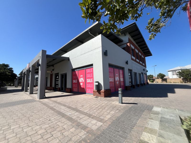 Modern retail storefront featuring a paved entrance area, large display windows, and contemporary architectural design with brick and rendered facade elements.