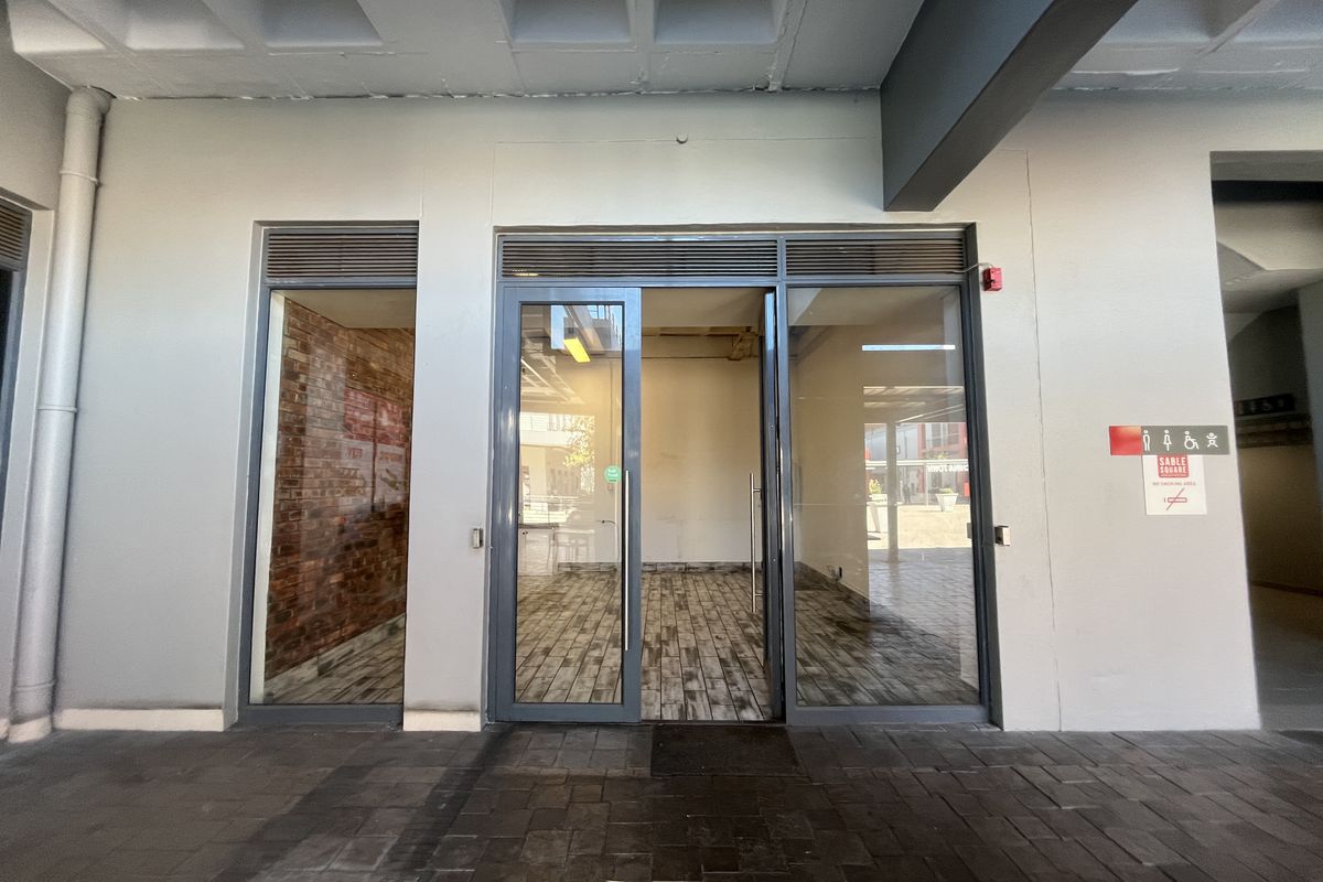 A modern retail storefront entrance featuring glass doors, wood-look tile flooring, and an exposed brick accent wall, providing a clean and professional commercial space.