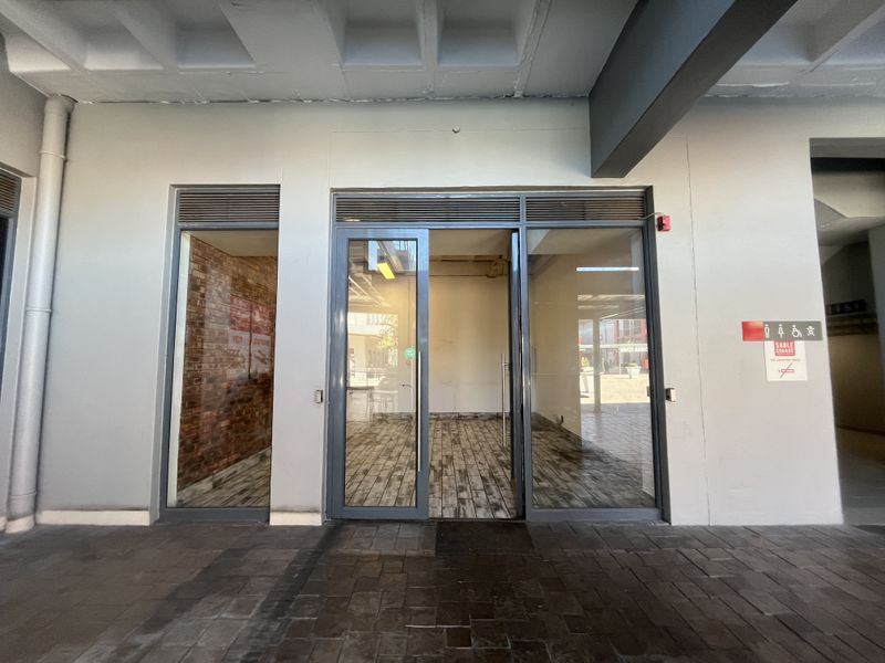A modern retail storefront entrance featuring glass doors, wood-look tile flooring, and an exposed brick accent wall, providing a clean and professional commercial space.