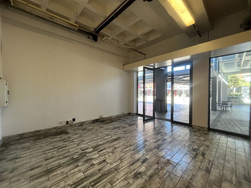 An empty open-plan retail space featuring exposed waffle slab ceilings, tiled flooring, and large glass storefront doors providing natural light and street access.