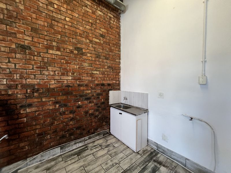A utility space featuring an exposed brick wall, tiled flooring, and a small sink unit with base cabinetry.