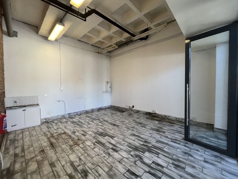 An empty utility or office space featuring a waffle slab ceiling, tiled flooring, and a small kitchenette unit with a glass entrance door.