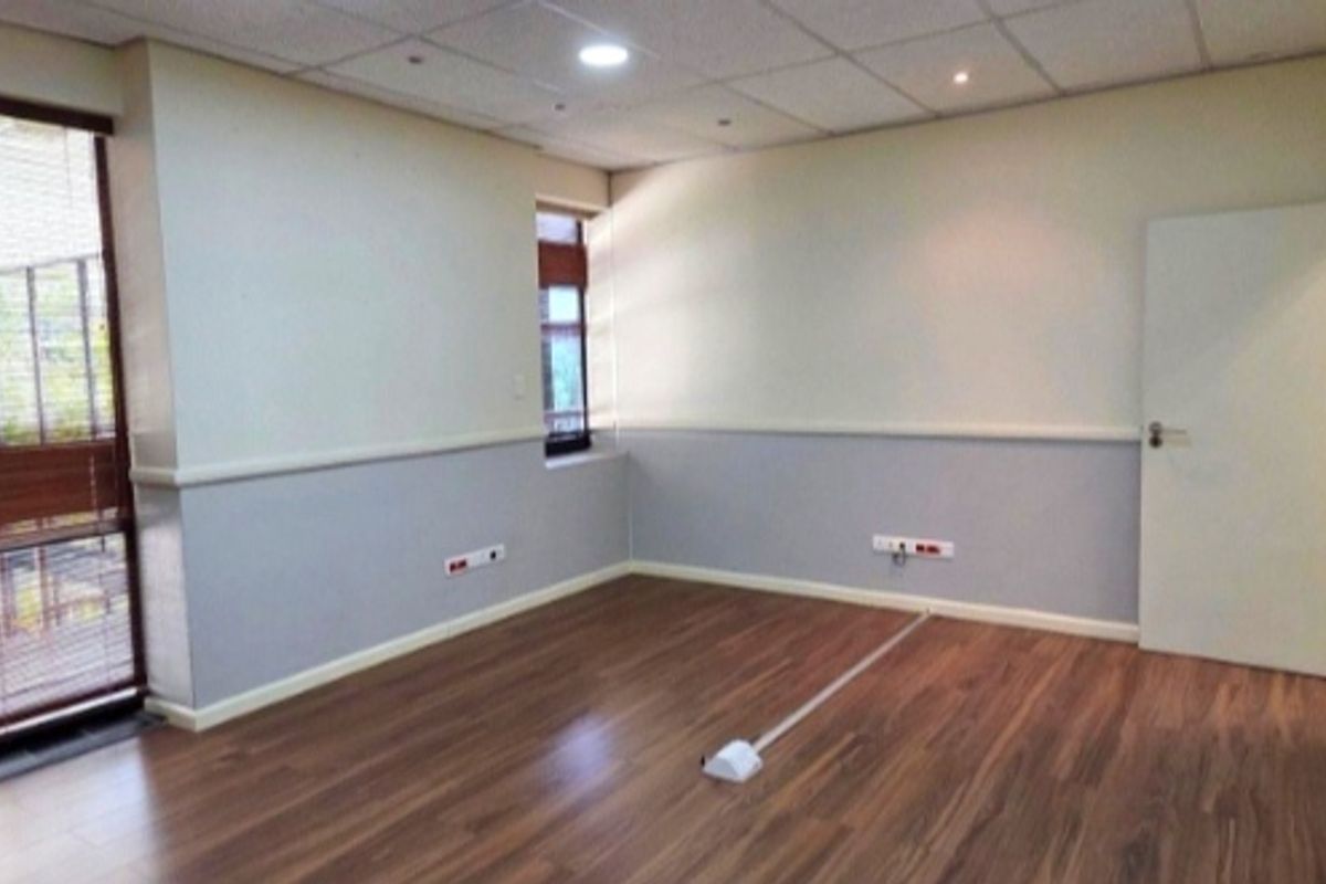 A clean, empty office space featuring laminate wood flooring, a drop ceiling with recessed lighting, and integrated electrical and data points.