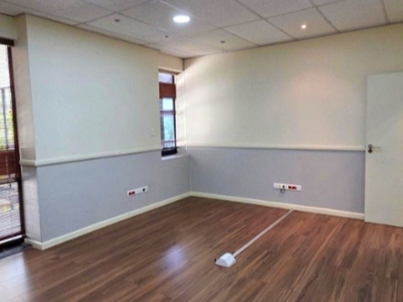 A clean, empty office space featuring laminate wood flooring, a drop ceiling with recessed lighting, and integrated electrical and data points.
