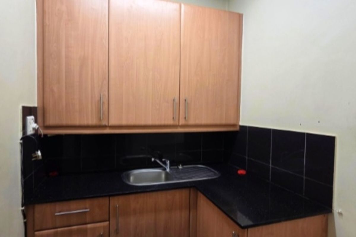 A compact office kitchenette featuring wood-look laminate cabinetry, a black granite countertop, and a stainless steel sink with a black tiled backsplash.