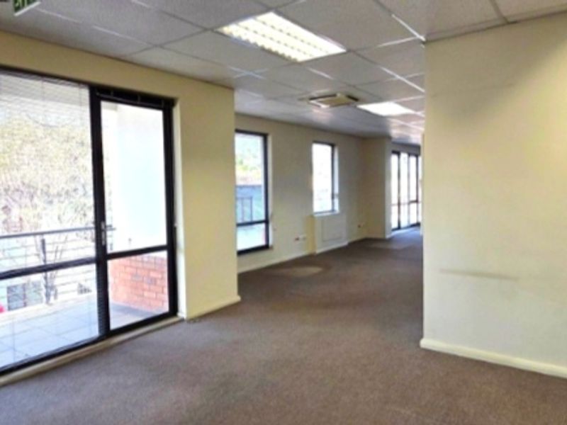 Spacious, open-plan office area featuring large windows, suspended ceilings with recessed lighting, and direct access to an outdoor balcony.