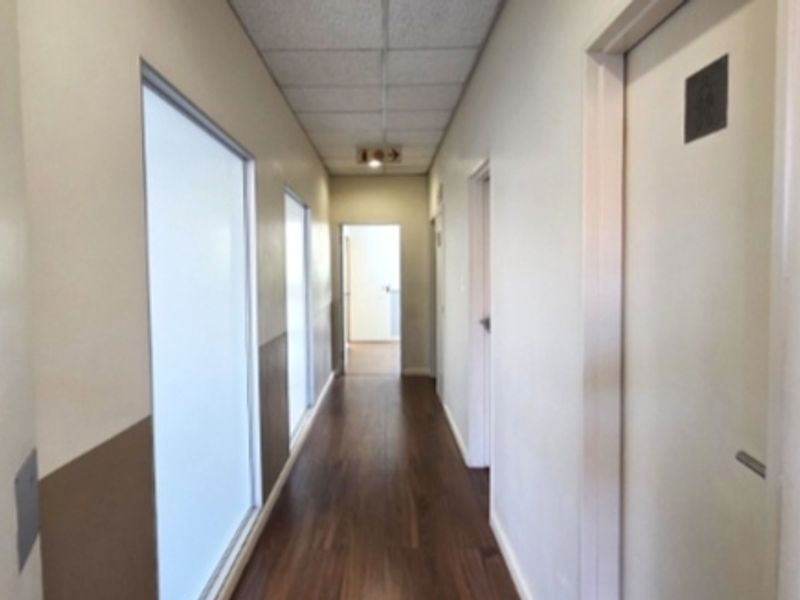 A clean, functional office hallway featuring laminate flooring, a suspended ceiling, and multiple internal access doors.