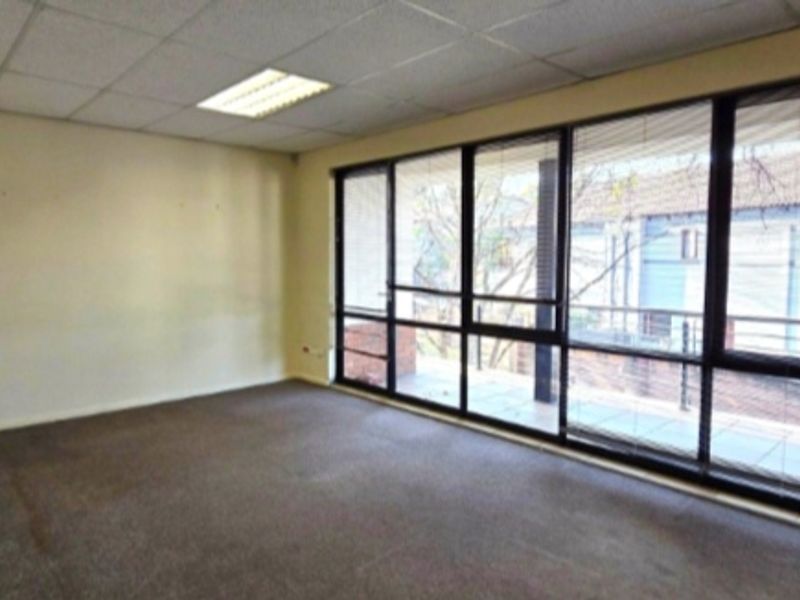 An empty office space featuring a suspended ceiling, recessed lighting, and large windows providing natural light and access to an exterior balcony.