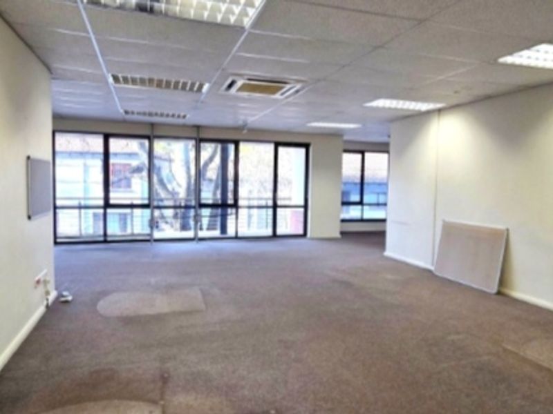 An open-plan office space featuring suspended ceilings, recessed lighting, air conditioning, and large windows providing natural light.