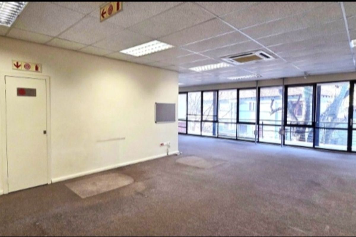 Spacious open-plan office area featuring large windows, suspended ceilings with recessed lighting, ducted air conditioning, and carpeted flooring.
