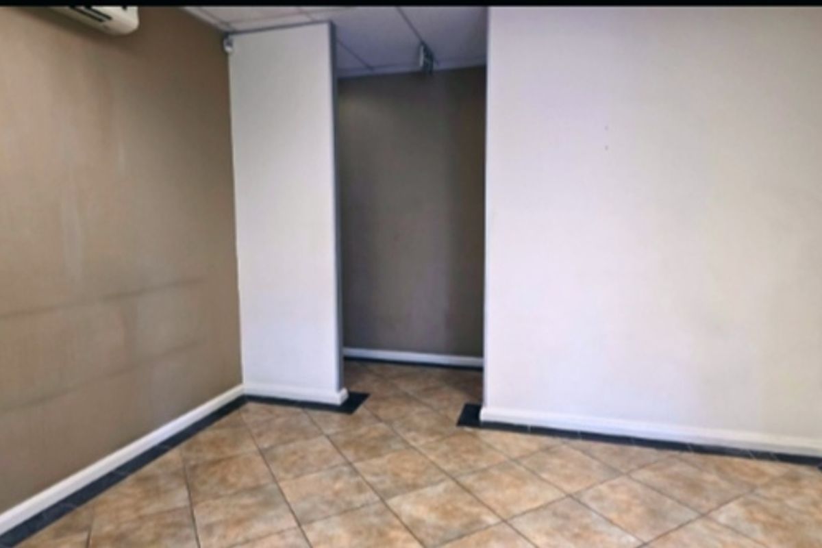 An empty office space featuring tiled flooring, a suspended ceiling, and an integrated air conditioning unit, ready for customization.
