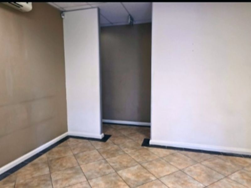 An empty office space featuring tiled flooring, a suspended ceiling, and an integrated air conditioning unit, ready for customization.