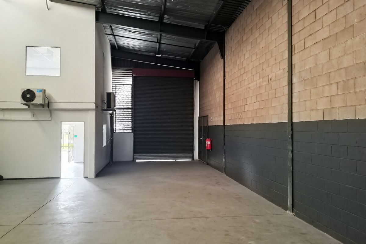 Spacious industrial warehouse unit featuring high ceilings, concrete flooring, a large roller shutter door, and integrated air conditioning.