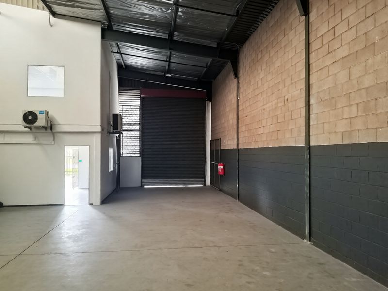 Spacious industrial warehouse unit featuring high ceilings, concrete flooring, a large roller shutter door, and integrated air conditioning.