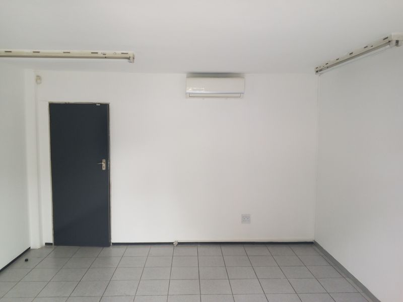 A clean, empty office space featuring tiled flooring, a wall-mounted split-system air conditioner, and functional overhead lighting.