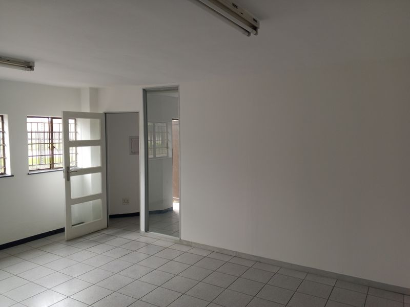 A clean, empty office space featuring tiled flooring, fluorescent lighting, and a glass panel door, suitable for a professional workspace.