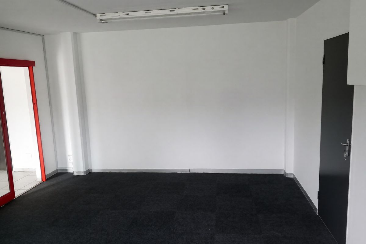 A clean, empty office space featuring dark carpet tiles, white walls, and a functional fluorescent light fixture.