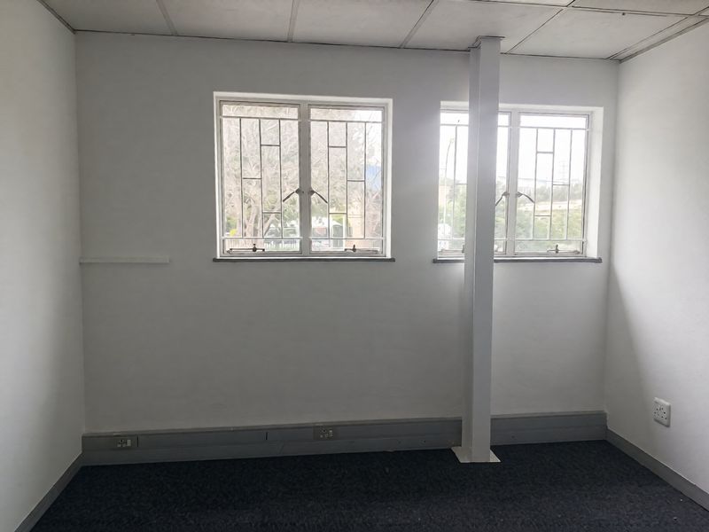 A vacant office space featuring carpeted flooring, a suspended ceiling, and windows fitted with security bars, providing a functional industrial workspace.