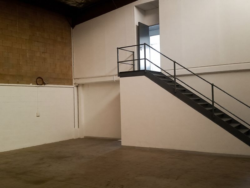 Spacious industrial utility area featuring concrete flooring, exposed blockwork walls, and a metal staircase providing access to an upper mezzanine level.