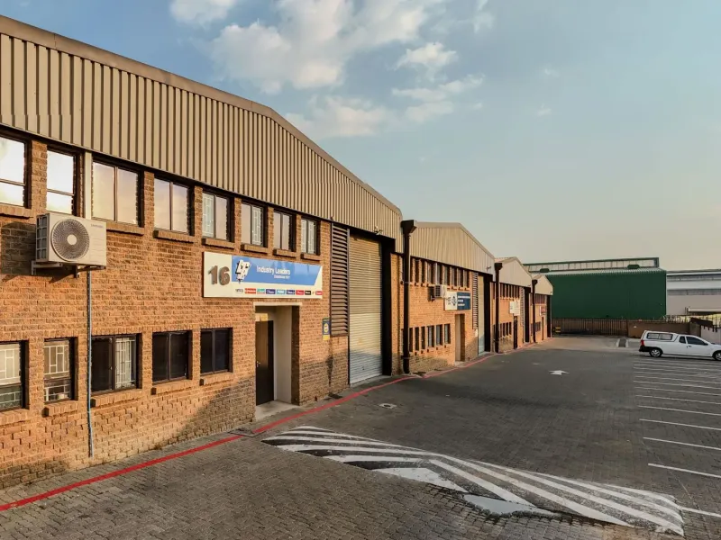 Front elevation of an industrial warehouse complex featuring brick construction, roller shutter access, and dedicated paved parking bays.