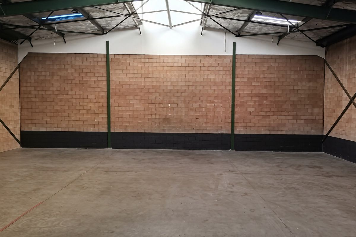 Spacious industrial utility area featuring exposed steel roof trusses, skylights, concrete flooring, and sturdy brick walls, suitable for various commercial or storage applications.