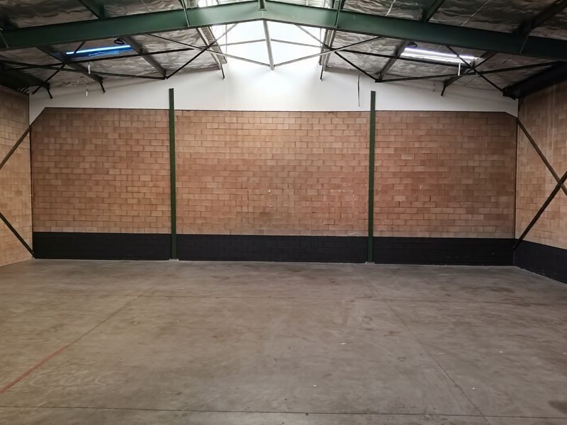 Spacious industrial utility area featuring exposed steel roof trusses, skylights, concrete flooring, and sturdy brick walls, suitable for various commercial or storage applications.