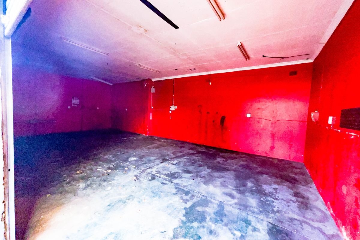An empty industrial utility space featuring concrete flooring, fluorescent lighting, and red painted walls, suitable for storage or workshop use.