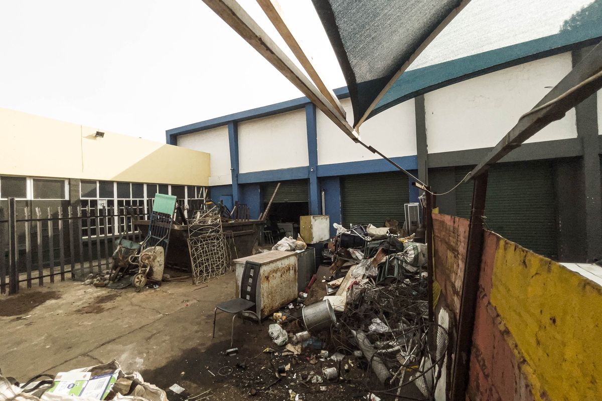 Rear industrial yard area featuring concrete paving, roller shutter access points, and overhead shade cloth structure, currently used for storage.