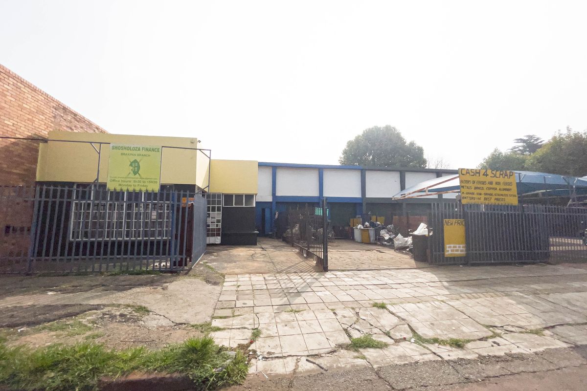 Front view of an industrial property featuring a paved driveway, steel security fencing, and commercial signage.