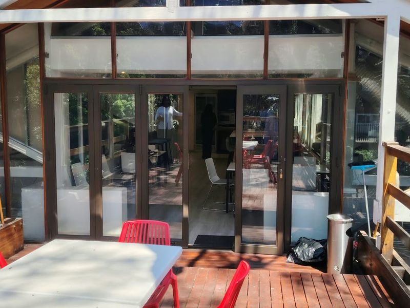 A spacious outdoor timber deck featuring a balustrade and large glass sliding doors providing access to the office interior.