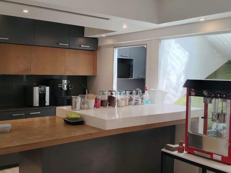 Modern office kitchen featuring sleek dark cabinetry, wood-toned accents, built-in appliances, and a spacious stone island countertop with integrated sink.