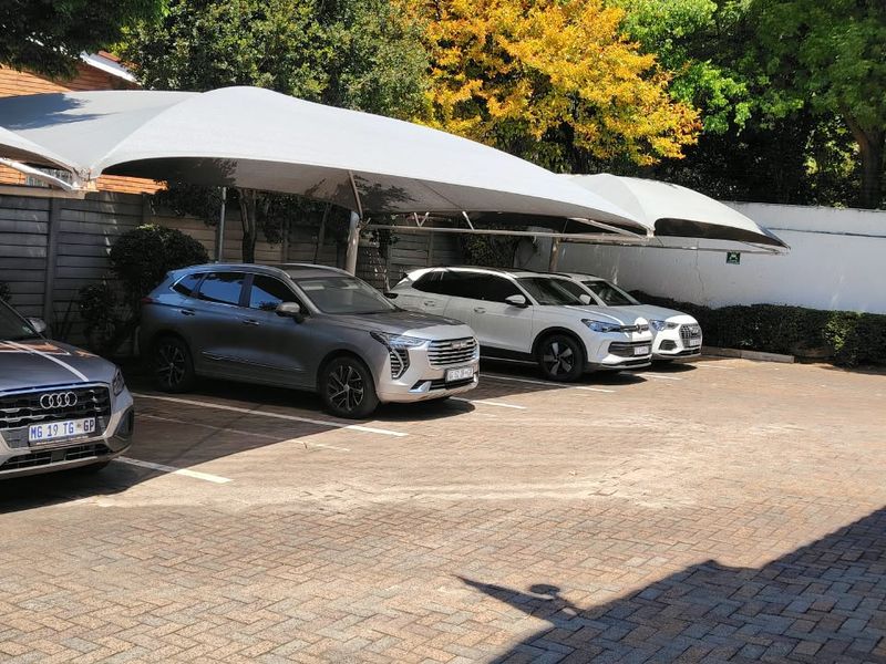 A paved outdoor parking area featuring multiple shade cloth carports and secure boundary walling.
