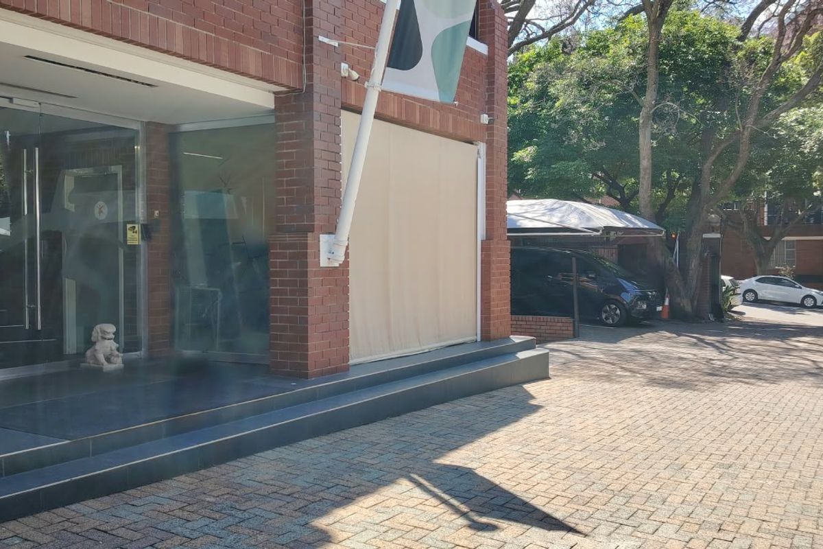 Front exterior view of a brick office building featuring a glass entrance, paved driveway, and covered parking area.