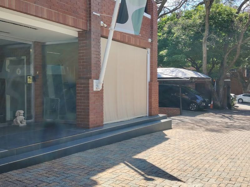 Front exterior view of a brick office building featuring a glass entrance, paved driveway, and covered parking area.