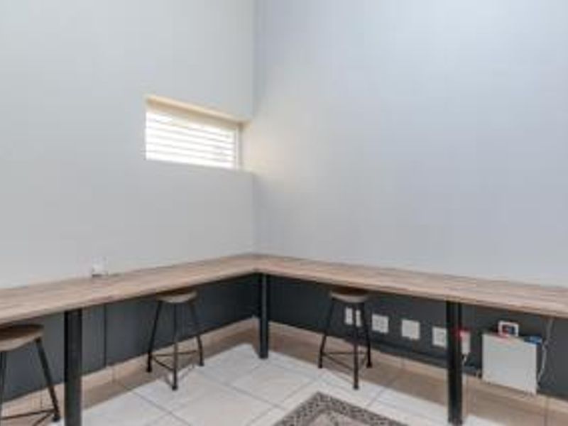 A functional office space featuring a wrap-around built-in desk, tiled flooring, and a high-level window providing natural light.