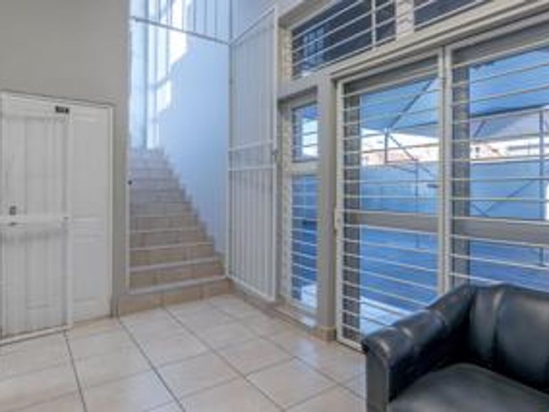 A functional entrance area featuring tiled flooring, a staircase, and secure metal security gates and window bars.