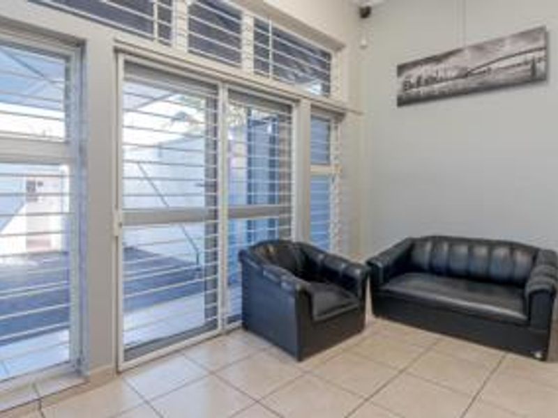 A bright living area featuring large sliding glass doors with security bars, transom windows, and neutral tiled flooring.