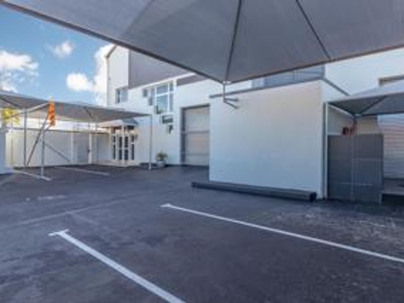 Exterior view of a commercial property featuring paved parking bays with shade cloth carports and roller shutter access doors.