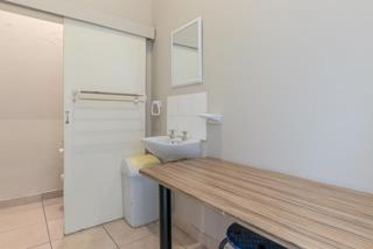 A functional bathroom featuring a wall-mounted basin, tiled flooring, and a sliding door, providing a clean and practical space.