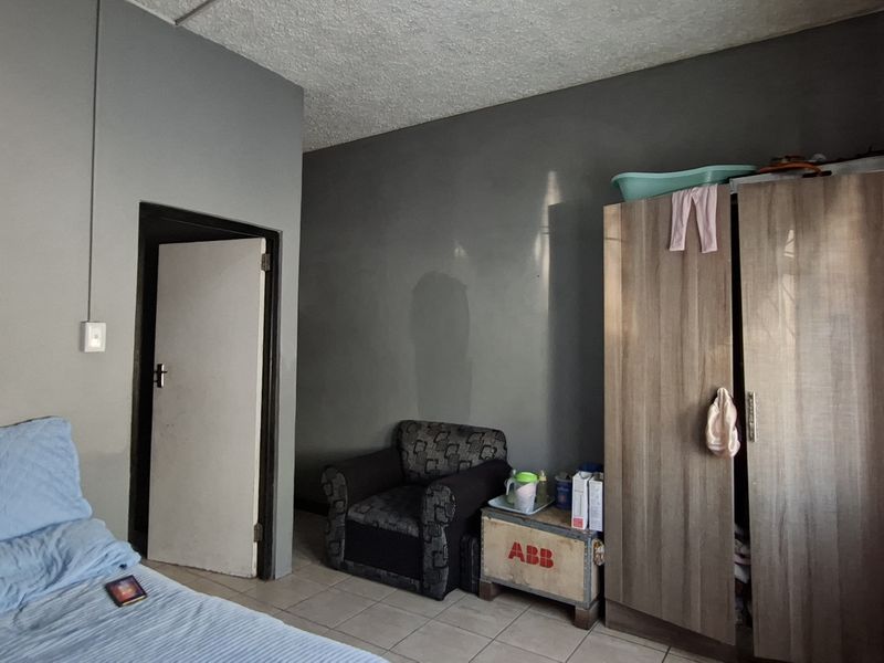 A bedroom featuring tiled flooring and textured ceiling, currently requiring cosmetic updates to the wall finishes and general maintenance.